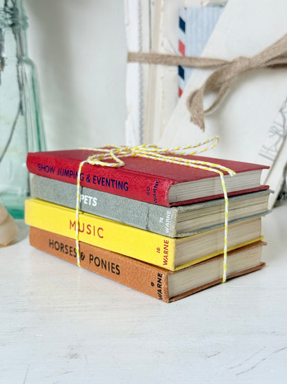 A stack of four vintage hardcover books tied with yellow string, placed on a white surface. The spines show titles including &