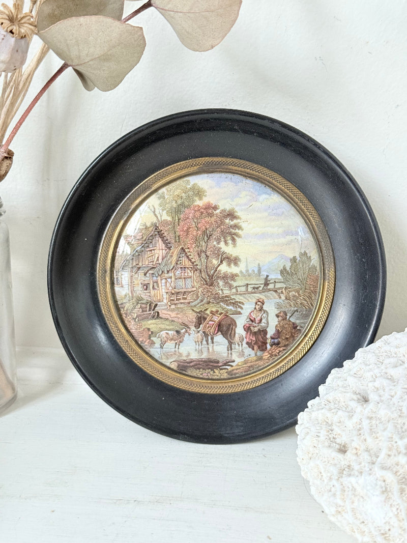 Antique Prattware framed pot lid with cottage scene photographed on a white surface.
