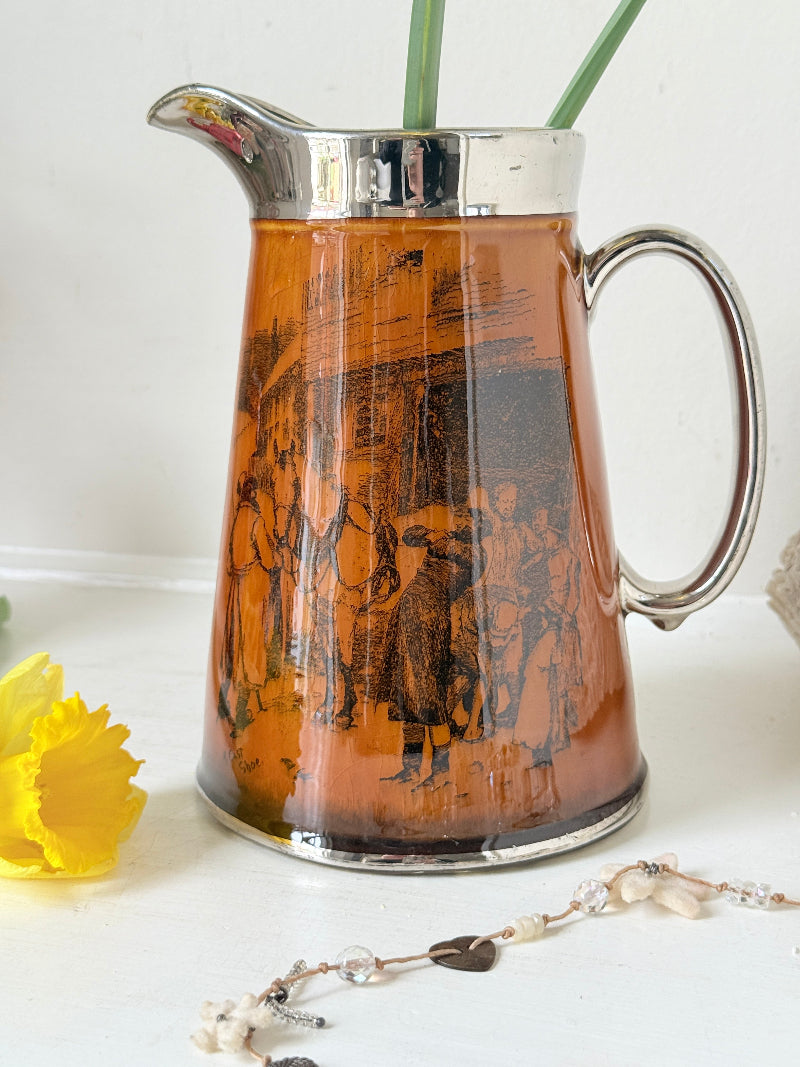 Antique Ridgways stoneware jug photographed on a white surface in amber treacle glaze with black Coaching Days and Coaching Ways scenes and silver lustre rim