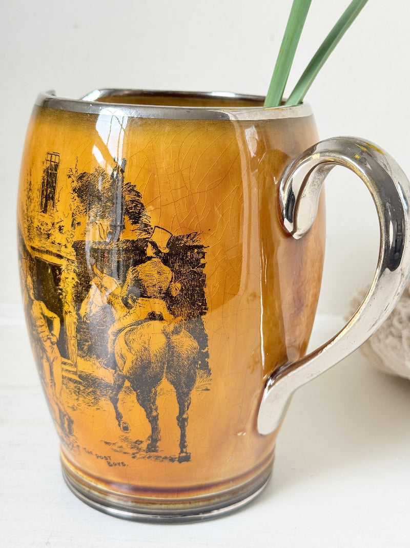 Antique Ridgways stoneware jug photographed on a white surface in amber treacle glaze with black Coaching Days and Coaching Ways transfer scenes and silver tone handle