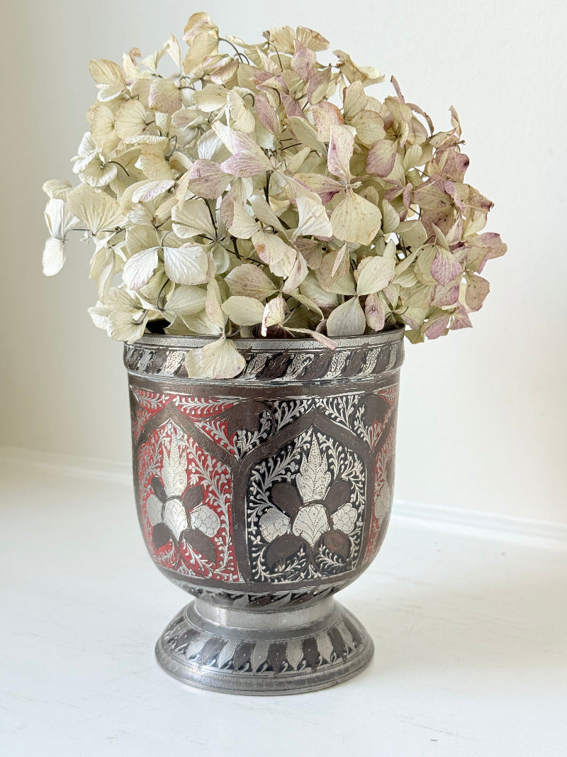 vintage indian metal lassi cup with red and white enamel motifs, styled with dried hydrangeas on a white surface