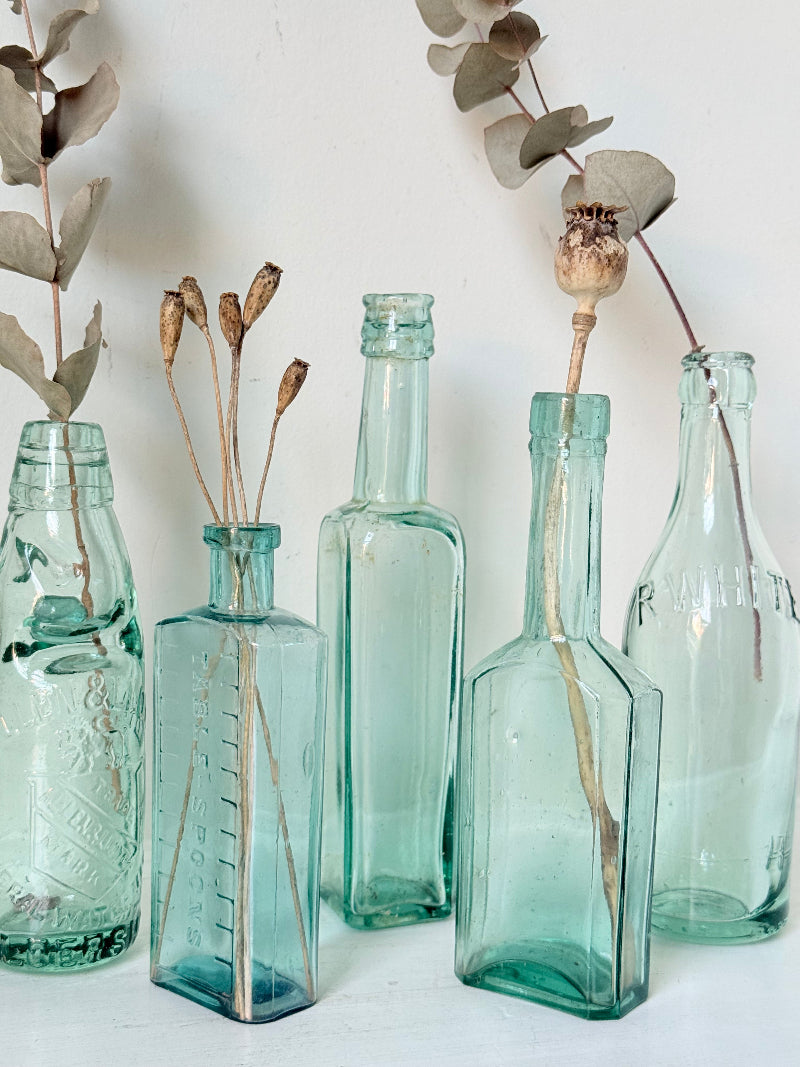 Set of five antique aqua green glass bottles with embossed lettering, photographed on a white surface