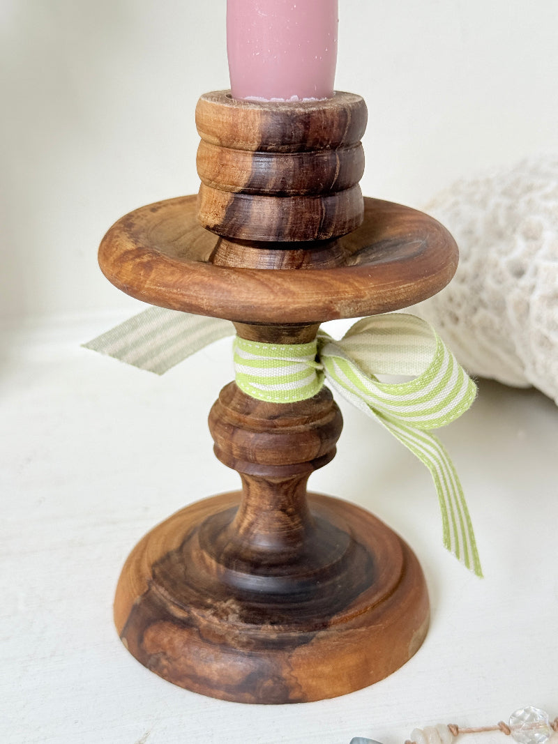 Vintage olivewood candlestick photographed on a white surface, turned wooden stem with warm grain and wide base holding a pink taper candle