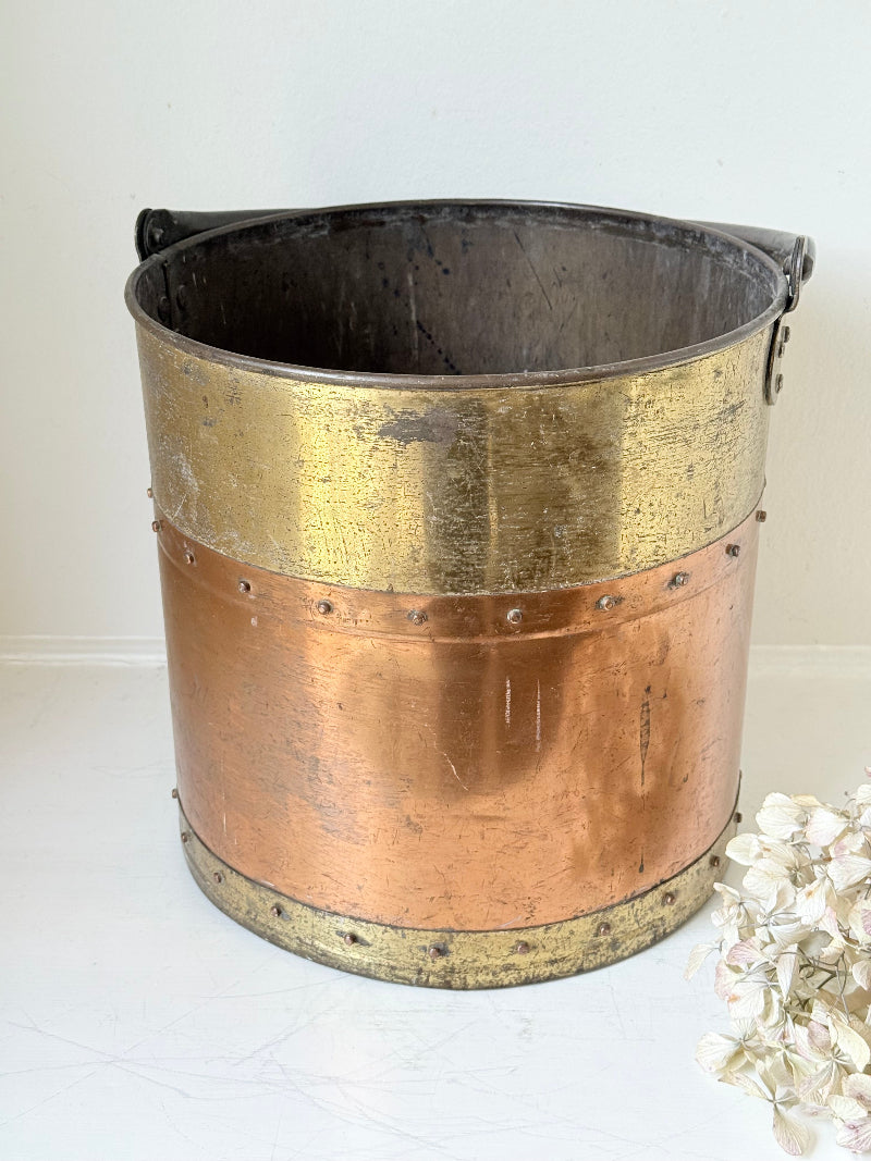 Vintage copper and brass metal bin with handle, photographed on a white surface.