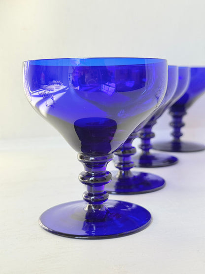 Set of four vintage cobalt blue cocktail glasses with stepped stems, photographed on a white surface