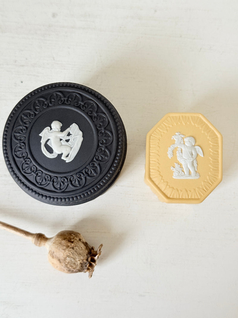 Pair of vintage Wedgwood Jasperware trinket pots in black and yellow with white relief decoration, photographed on a white surface