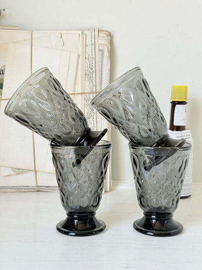 Set of four smoke grey pressed glass footed goblets with a diamond pattern, photographed on a white surface