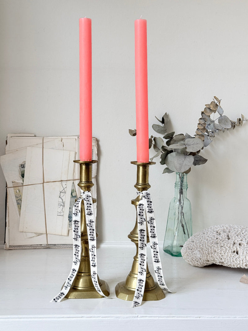 Pair of antique brass candlesticks with turned baluster stems and stepped bases holding coral tapers