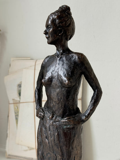 Solid bronze figure of a standing semi nude woman with upswept hair on a white marble base