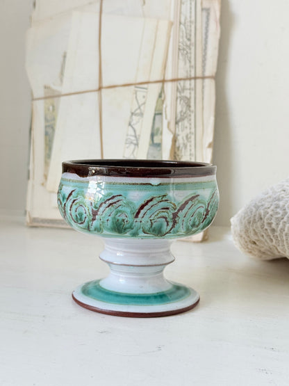 Hand thrown studio pottery footed bowl with green and brown swirling decoration photographed on a white surface
