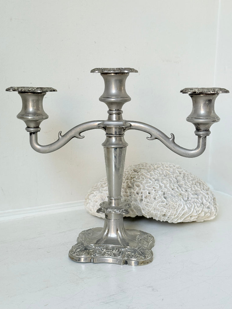 Vintage silver coloured three-arm candelabra with ornate base and soft patina, photographed on a white surface