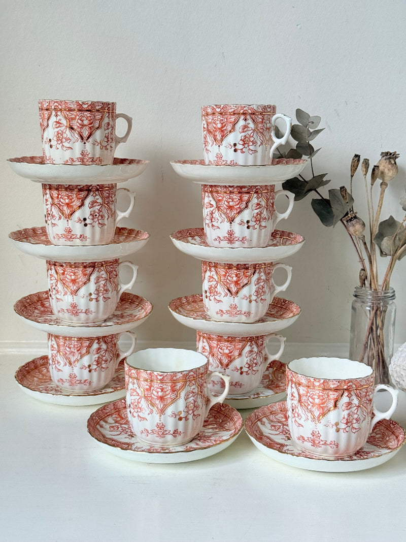 Vintage coral transferware coffee cans and saucers with scalloped edges and gold accents, set of ten, styled on a white surface.