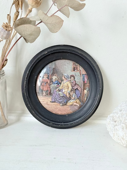 Antique Prattware pot lid in black round frame with Victorian family scene on white surface.