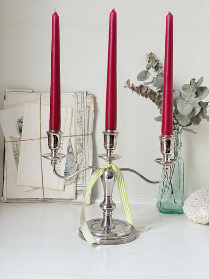 Silver plate three light candelabra with curved arms and domed base holding red taper candles