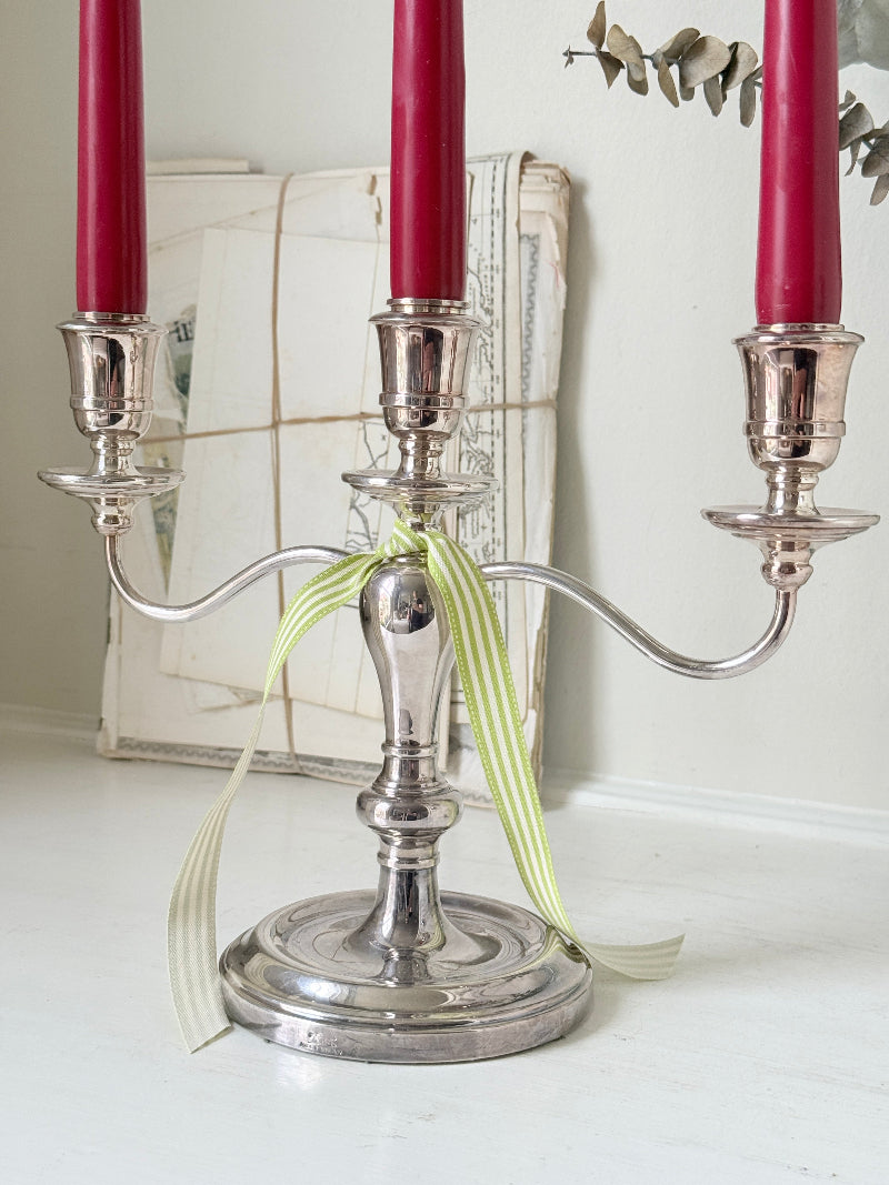 Silver plate three light candelabra with curved arms and domed base holding red taper candles