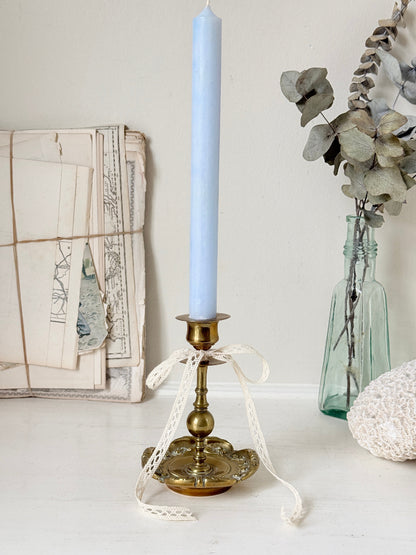Brass candlestick with turned baluster stem and scalloped embossed base photographed on a white surface