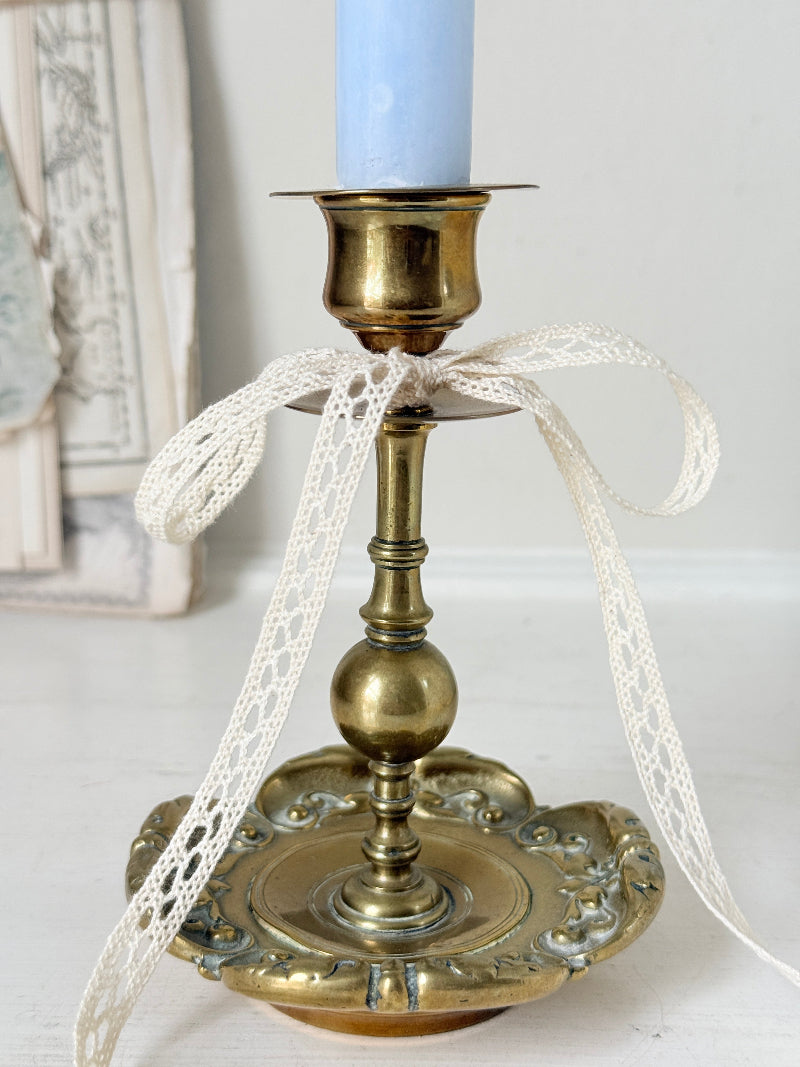 Brass candlestick with turned baluster stem and scalloped embossed base photographed on a white surface