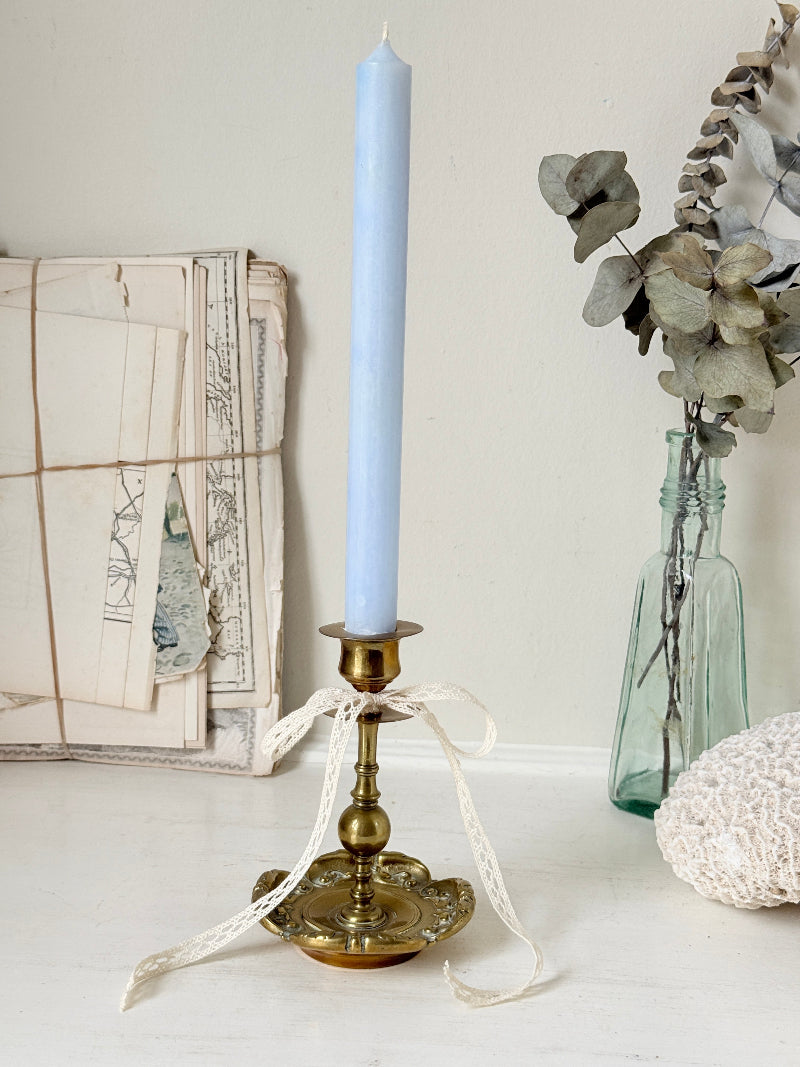 Brass candlestick with turned baluster stem and scalloped embossed base photographed on a white surface