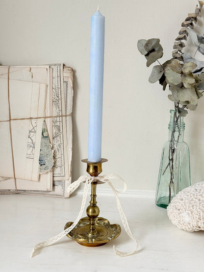 Brass candlestick with turned baluster stem and scalloped embossed base photographed on a white surface