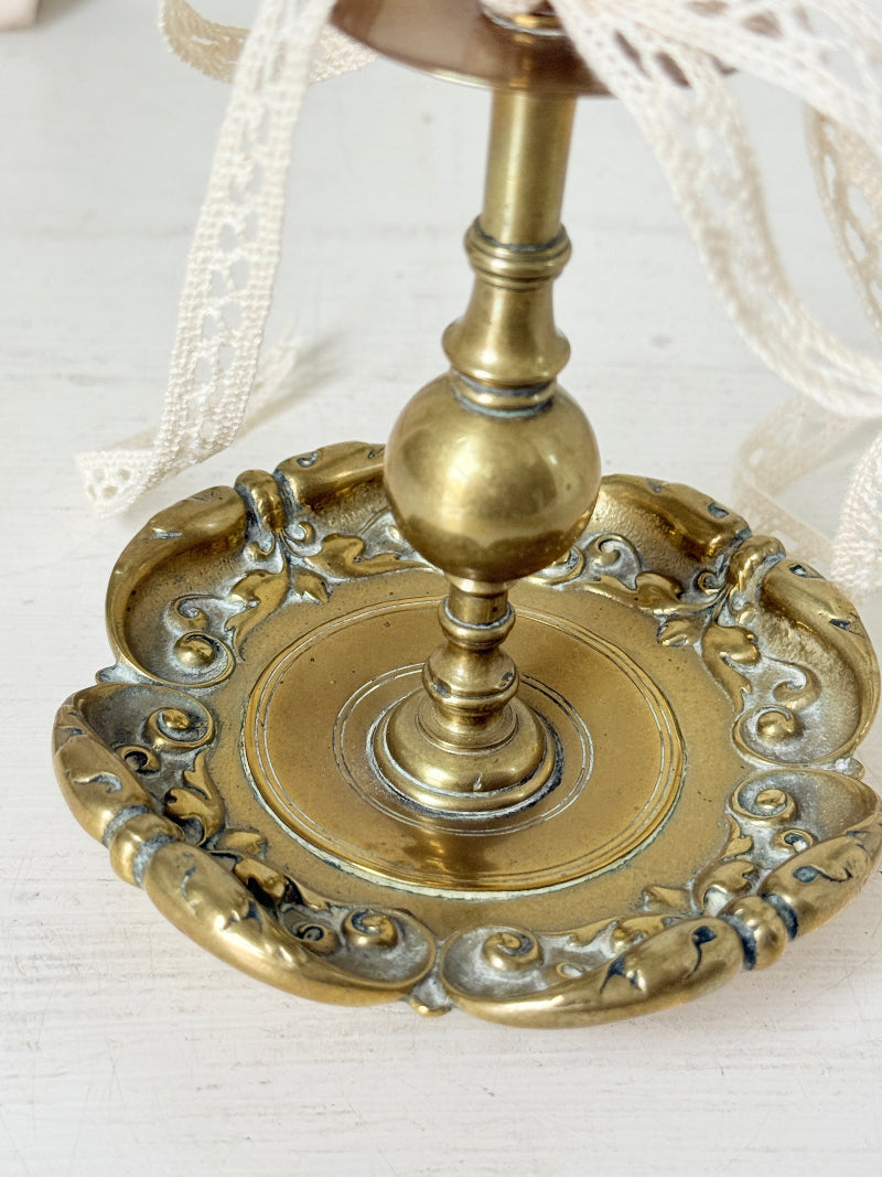 Brass candlestick with turned baluster stem and scalloped embossed base photographed on a white surface