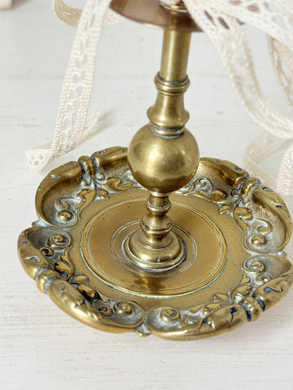 Brass candlestick with turned baluster stem and scalloped embossed base photographed on a white surface
