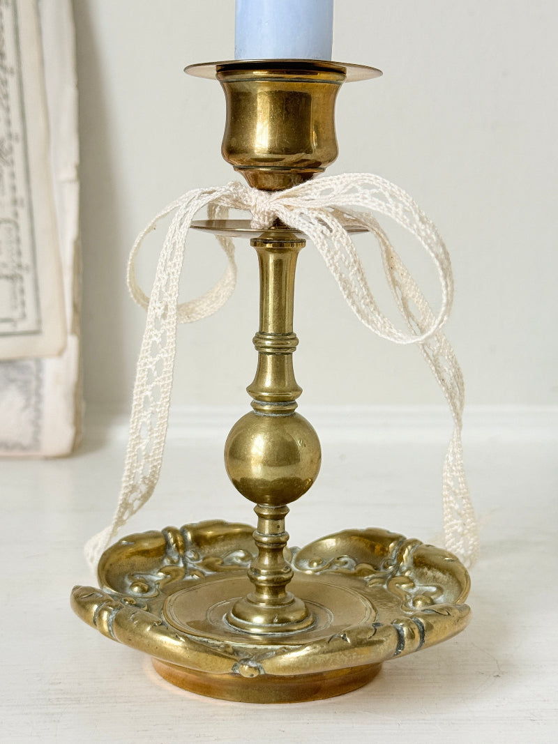 Brass candlestick with turned baluster stem and scalloped embossed base photographed on a white surface