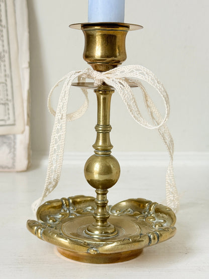 Brass candlestick with turned baluster stem and scalloped embossed base photographed on a white surface