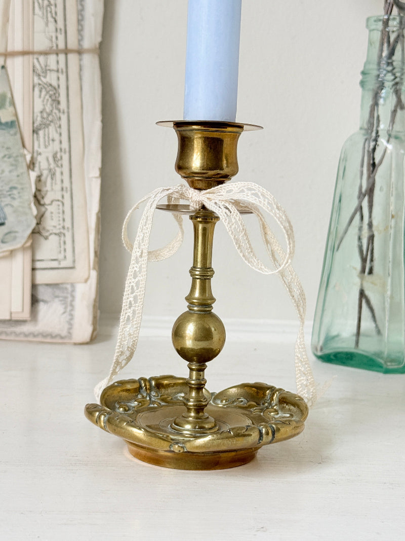Brass candlestick with turned baluster stem and scalloped embossed base photographed on a white surface