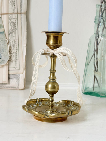 Brass candlestick with turned baluster stem and scalloped embossed base photographed on a white surface