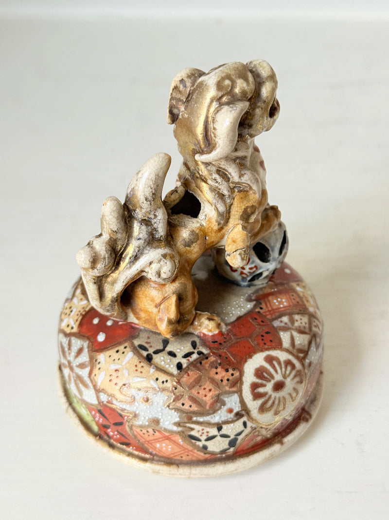 An antique Japanese ceramic figurine of a dog standing on a decorated round base, photographed against a plain off-white background.