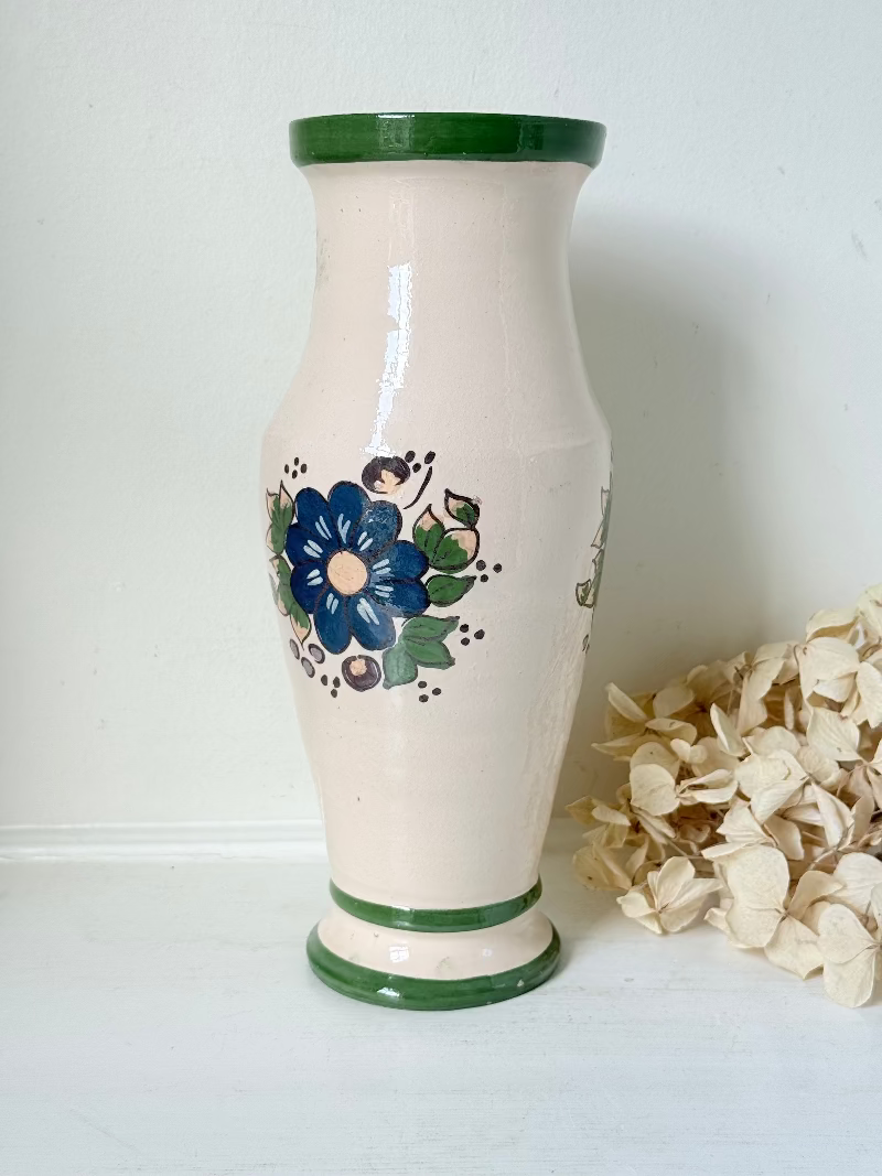 Vintage studio pottery vase with hand painted blue floral design and green glazed rim and foot, photographed on white surface.