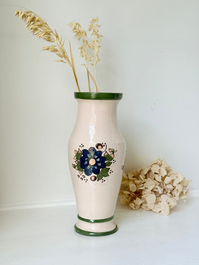 Vintage studio pottery vase with hand painted blue floral design and green glazed rim and foot, photographed on white surface.