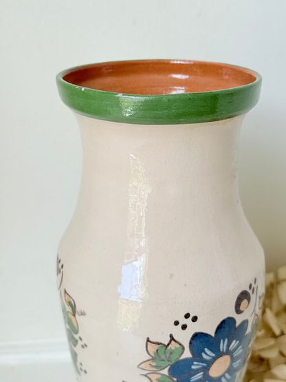 Vintage studio pottery vase with hand painted blue floral design and green glazed rim and foot, photographed on white surface.
