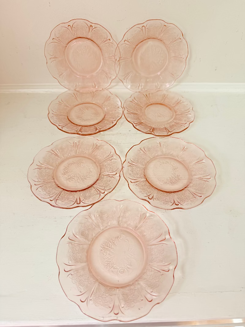 Set of seven vintage pressed glass coral plates with cherry and blossom motif, photographed on white surface.