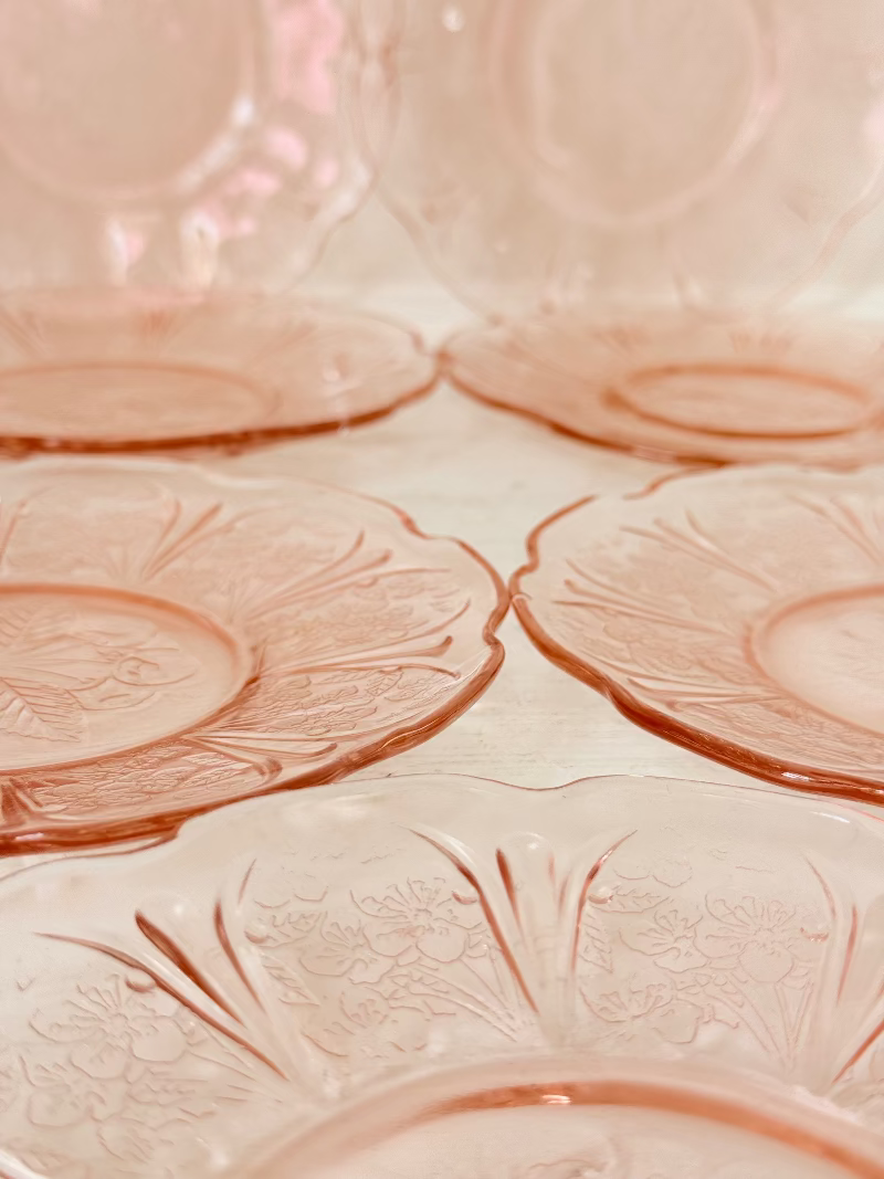 Set of seven vintage pressed glass coral plates with cherry and blossom motif, photographed on white surface.