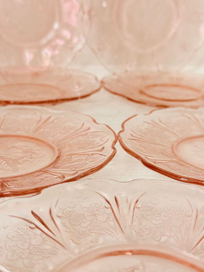 Set of seven vintage pressed glass coral plates with cherry and blossom motif, photographed on white surface.