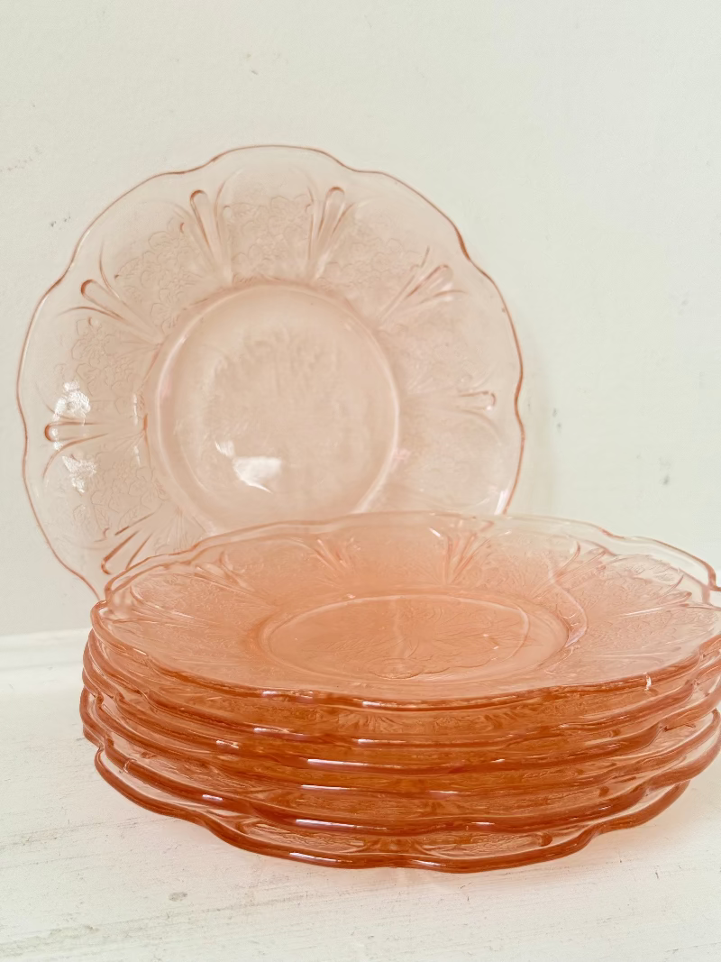 Set of seven vintage pressed glass coral plates with cherry and blossom motif, photographed on white surface.