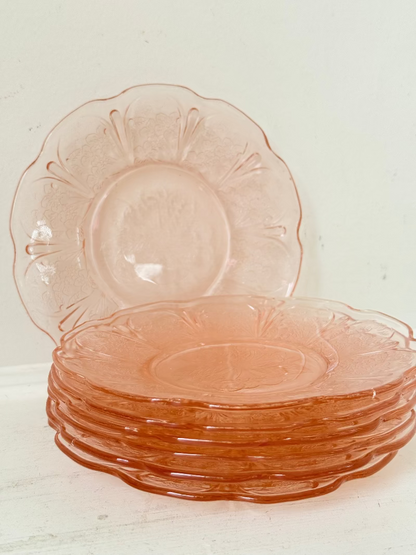 Set of seven vintage pressed glass coral plates with cherry and blossom motif, photographed on white surface.