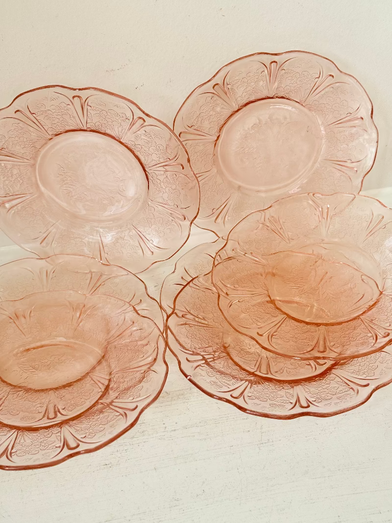 Set of seven vintage pressed glass coral plates with cherry and blossom motif, photographed on white surface.
