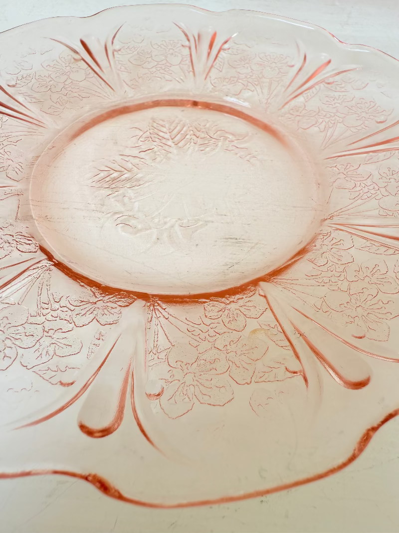 Set of seven vintage pressed glass coral plates with cherry and blossom motif, photographed on white surface.