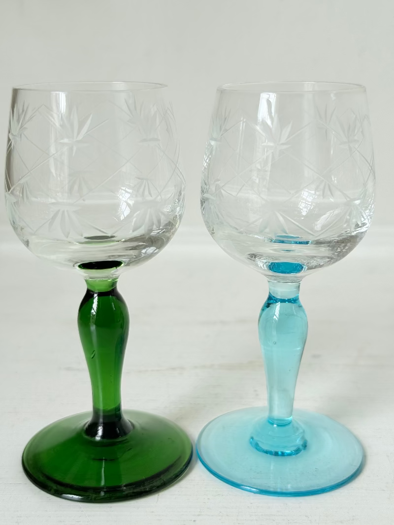 Vintage set of four etched liqueur glasses with colourful stems in green, amber, blue, and turquoise, photographed on a white surface
