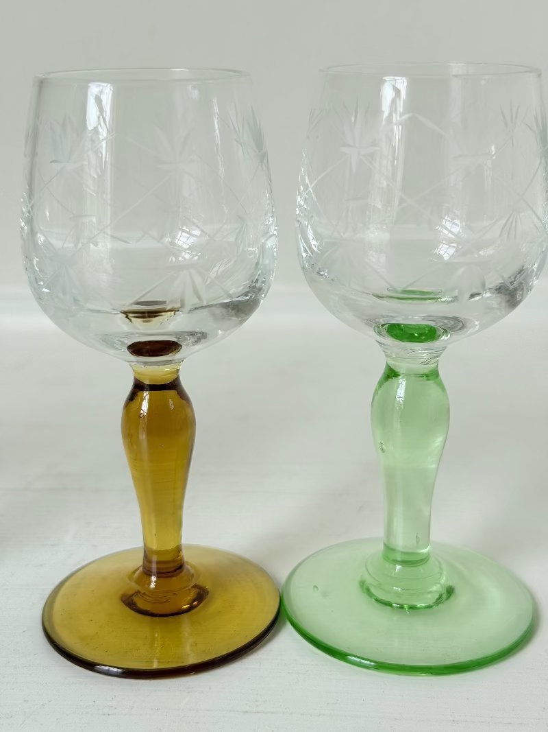 Vintage set of four etched liqueur glasses with colourful stems in green, amber, blue, and turquoise, photographed on a white surface