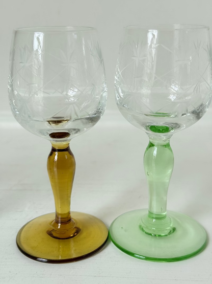 Vintage set of four etched liqueur glasses with colourful stems in green, amber, blue, and turquoise, photographed on a white surface