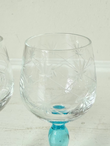 Vintage set of four etched liqueur glasses with colourful stems in green, amber, blue, and turquoise, photographed on a white surface