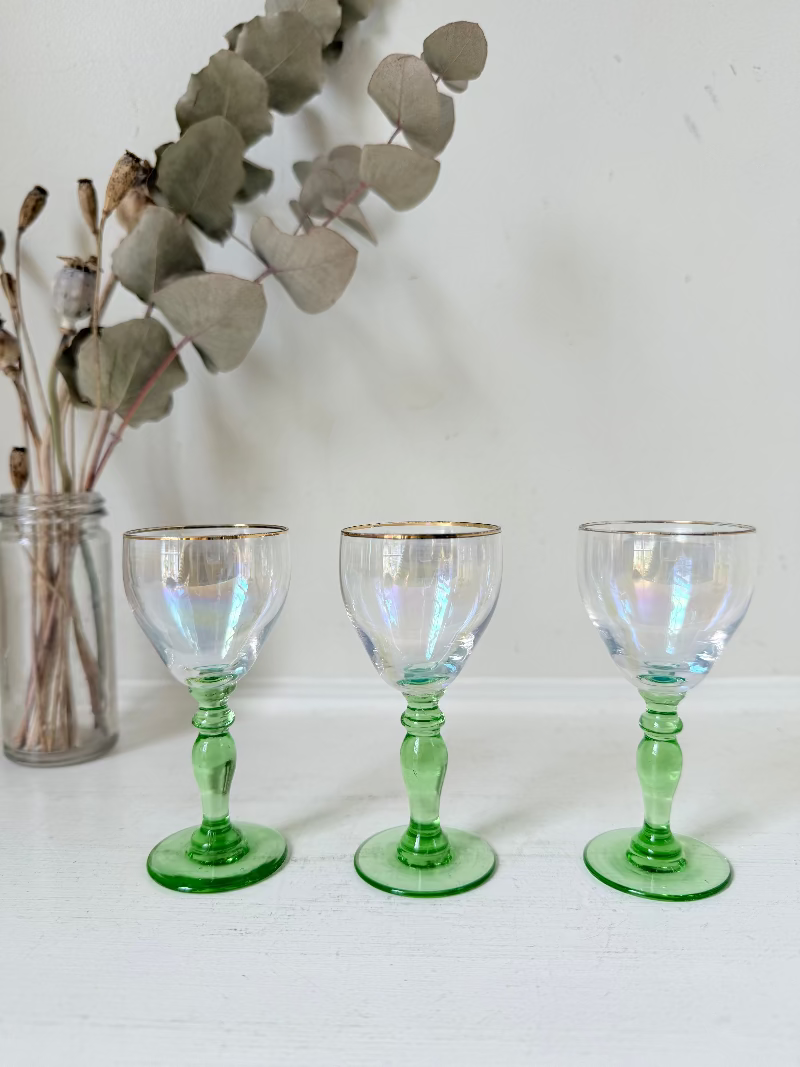 Vintage trio of iridescent shot glasses with green stems and gilt rims, photographed on a white surface