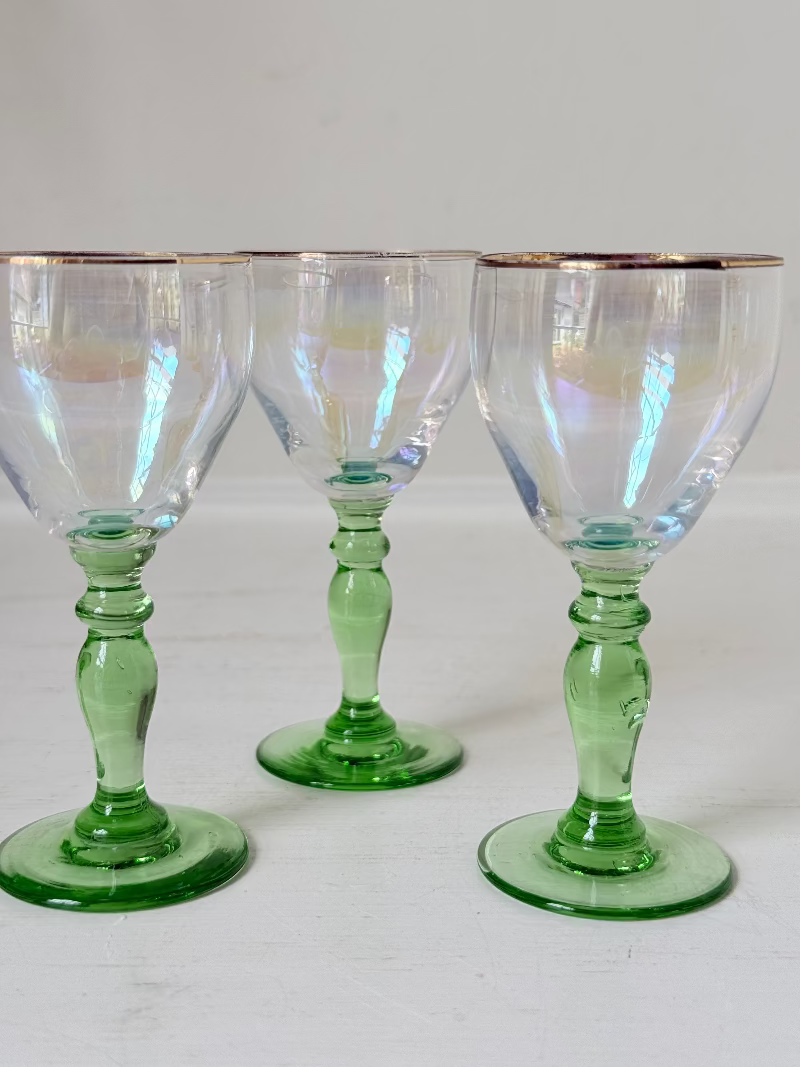 Vintage trio of iridescent shot glasses with green stems and gilt rims, photographed on a white surface