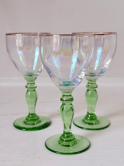 Vintage trio of iridescent shot glasses with green stems and gilt rims, photographed on a white surface