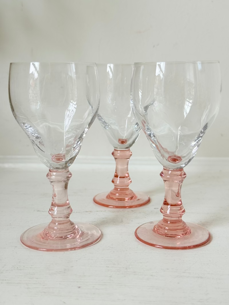 Set of three vintage liquor glasses with clear bowls and pink stems, one paler in tone, photographed on white surface.