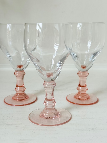 Set of three vintage liquor glasses with clear bowls and pink stems, one paler in tone, photographed on white surface.