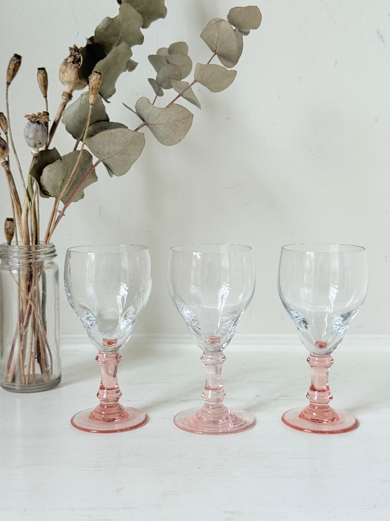 Set of three vintage liquor glasses with clear bowls and pink stems, one paler in tone, photographed on white surface.